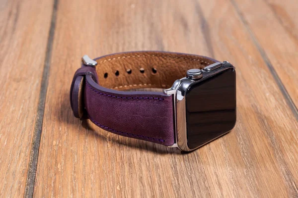 Ahşap zemindeki akıllı saate bağlı mor deri kayış..