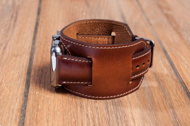 Tahta zemindeki akıllı saate bağlı kahverengi deri kayış..