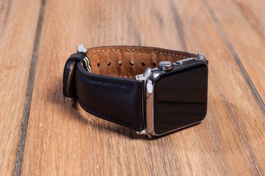 Ahşap zemindeki akıllı saate bağlı siyah deri kayış..