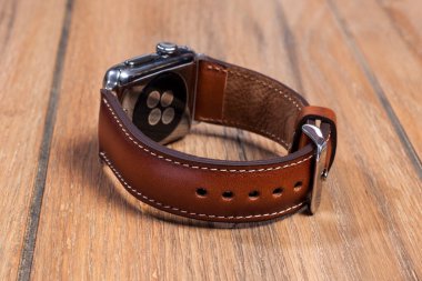 Tahta zemindeki akıllı saate bağlı kahverengi deri kayış..