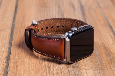 Tahta zemindeki akıllı saate bağlı kahverengi deri kayış..