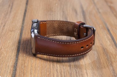 Tahta zemindeki akıllı saate bağlı kahverengi deri kayış..