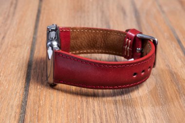 Ahşap zemindeki akıllı saate bağlı kırmızı deri kayış..