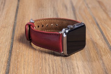 Ahşap zemindeki akıllı saate bağlı kırmızı deri kayış..