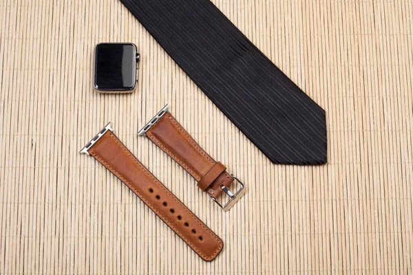 Smart watch, leather strap and tie on light wood floor