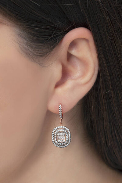 Silver dangly earrings attached to a groomed lady's ear. Jewelry image that can be used in e-commerce sales.