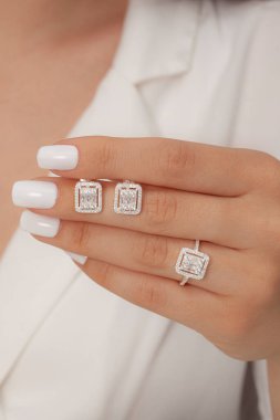 Güzelce döşenmiş tırnakları olan güzel bir mücevher seti sunuyor. Kolye, küpe ve yüzük gümüş, elmas, altın.