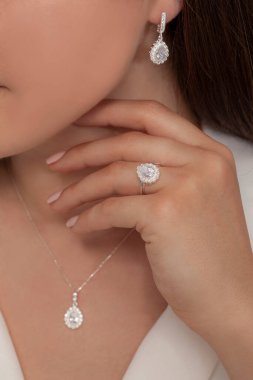 Güzelce döşenmiş tırnakları olan güzel bir mücevher seti sunuyor. Kolye, küpe ve yüzük gümüş, elmas, altın.