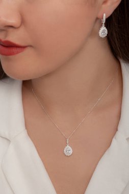 Beyaz elbiseli bayanın taktığı yuvarlak taşlı elmas takılar..