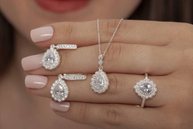 Güzelce döşenmiş tırnakları olan güzel bir mücevher seti sunuyor. Kolye, küpe ve yüzük gümüş, elmas, altın.