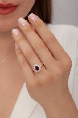 Kahverengi saçlı, bakımlı elleri beyaz elbiseli, şarap rengi ve damla şeklinde elmas yüzüklü genç bir manken..