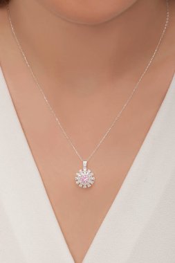 Beyaz elbiseli kahverengi saçlı kadın manken çiçek şeklinde pembe elmas kolyeyle poz veriyor. İnternette satılık.