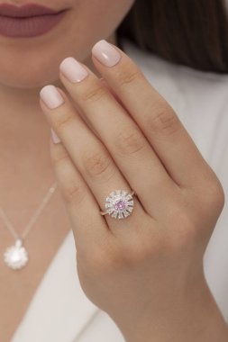 Kahverengi saçlı ve beyaz elbiseli çıplak tırnak cilası olan genç bir kadın parmağında çiçek şeklinde bir elmas yüzük gösteriyor. İnternette satılık.
