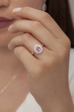 Kahverengi saçlı beyaz elbiseli kadın çıplak tırnak cilası ile poz veriyor, pembe elmas yüzük takıyor..