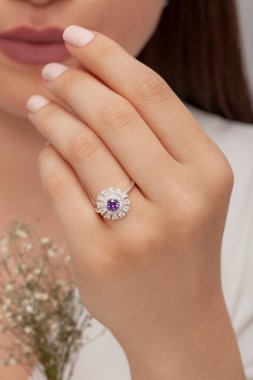 Beyaz elbiseli, beyaz çiçekli, bakımlı kadın model, yuvarlak elmas bir yüzükle poz veriyor..