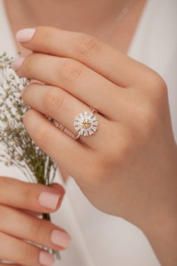 Beyaz elbiseli, beyaz çiçekli, bakımlı kadın model, yuvarlak elmas bir yüzükle poz veriyor..