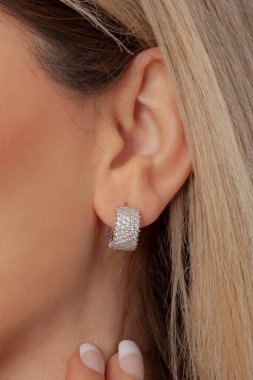 Bakımlı bir kadın kulağında gümüş küpeler gösteriyor. Çevrimiçi satışlar için küpe resmi.