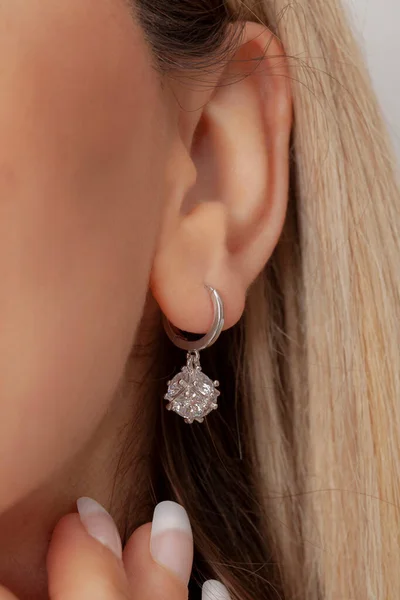 well-groomed woman shows silver earrings in her ear. Earring image for online sales.