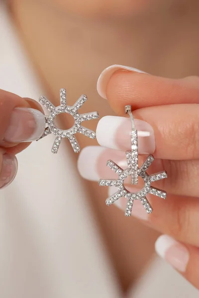 Woman showing silver earrings on her manicured well-groomed hands. Earring image for online sales.