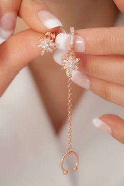 Manikürlü, bakımlı ellerinde gümüş küpeler gösteren bir kadın. Çevrimiçi satışlar için küpe resmi.