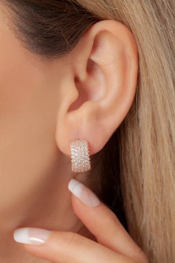 Sarışın kadın model, bakımlı eliyle elmas kaplamalı altın küpeleriyle poz veriyor. İnternette satılık.