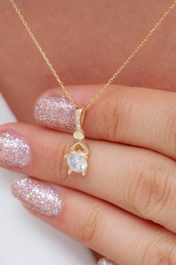 Elinde parlak ojeli bir kızın gümüş zarif kolyesi.