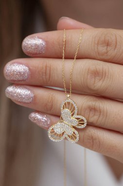 Elinde parlak ojeli bir kızın gümüş zarif kolyesi.