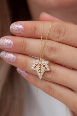 Elinde parlak ojeli bir kızın gümüş zarif kolyesi.