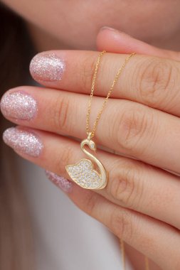 Elinde parlak ojeli bir kızın gümüş zarif kolyesi.