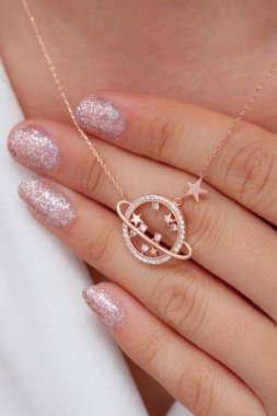 Elinde parlak ojeli bir kızın gümüş zarif kolyesi.