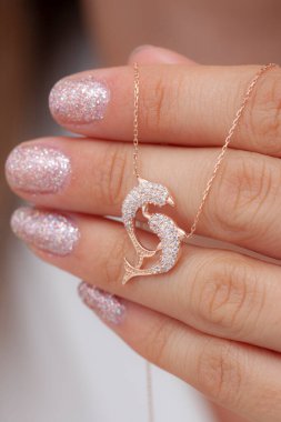 Elinde parlak ojeli bir kızın gümüş zarif kolyesi.