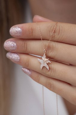 Elinde parlak ojeli bir kızın gümüş zarif kolyesi.