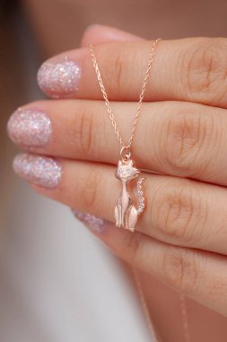 Elinde parlak ojeli bir kızın gümüş zarif kolyesi.