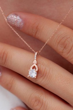 Elinde parlak ojeli bir kızın gümüş zarif kolyesi.