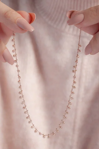 ピンクのセーターの女の子は よく手入れされた手で銀のチェーンを保持しています オンライン販売のためのネックレス画像 — ストック写真