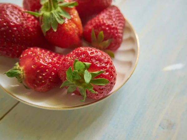 çilek beyaz bir tabak içinde. Ahşap arka plan üzerinde çilek plakadır