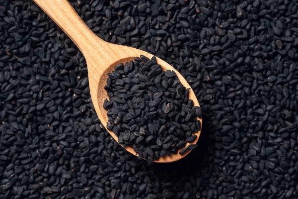 Black cumin seeds on wooden spoon on wooden background.