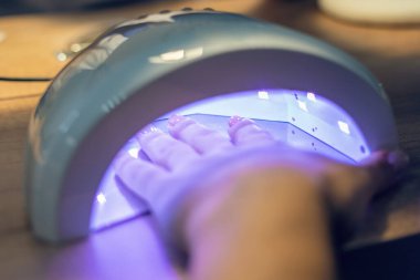 Kız, mor ötesi lamba kullanarak jöle cilasıyla tırnaklarını kurutuyor..