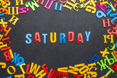 Siyah arka planda parlak renkli harflerden oluşan cumartesi kelimesi.