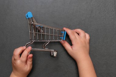 Çocuk elleri gri arka planda oyuncak alışveriş arabasını tutar.