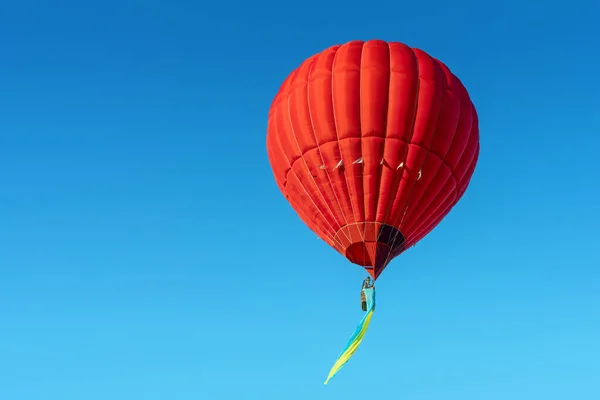Red hot air balloon with the flag of Ukraine on a blue sky background.