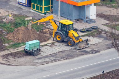 Sarı tekerlekli kazıcı şehirde bir çukur kazıyor..