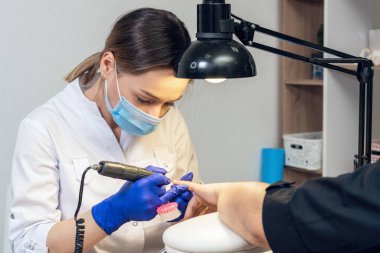 Manikürcü, bir manikürcüde elektrikli fren aleti kullanarak müşterinin elindeki ojeleri temizler..