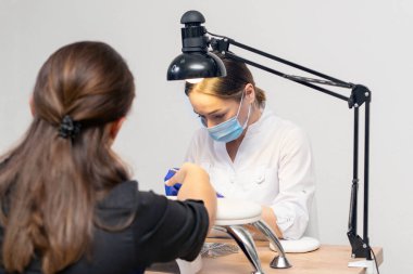 Manikürcü manikürcüde manikür yapıyor. Tırnak törpüsü kullanıyor..