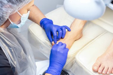 Pedikür uzmanı kuaförde tırnak törpüsü kullanarak pedikür yapıyor..