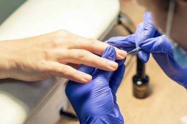 Manikürcü bir manikürcüde manikür yapıyor, tırnaklarına oje sürüyor..