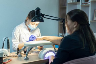 Manikürcü bir manikürcüde manikür yapıyor, tırnaklarına oje sürüyor..