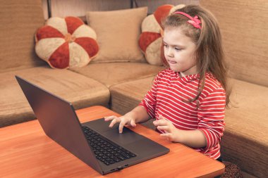 Gülümseyen küçük kız bilgisayarını uzaktan öğrenme ya da eğlence için kullanıyor..