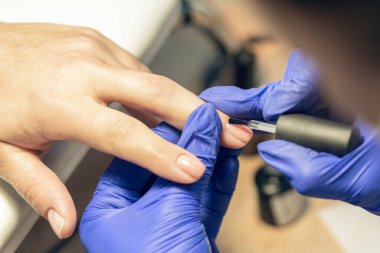 Manikürcü bir manikürcüde manikür yapıyor, tırnaklarına oje sürüyor..