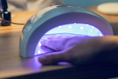 Kız, mor ötesi lamba kullanarak jöle cilasıyla tırnaklarını kurutuyor..